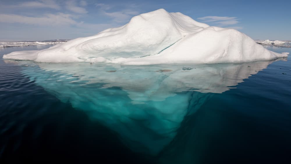An iceberg with its underside exposed in clear Arctic water